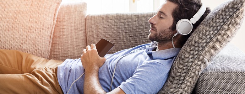 A young man lying on a sofa listening to music through headphones