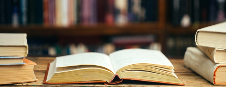 An open book on a desk in front of lined bookshelves