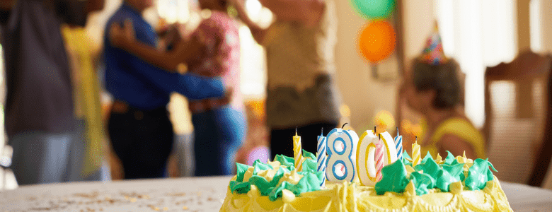 An 80th birthday cake with elderly guests celebrating in the background