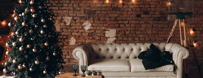 A decorated Christmas tree and a sofa against a bare brick wall