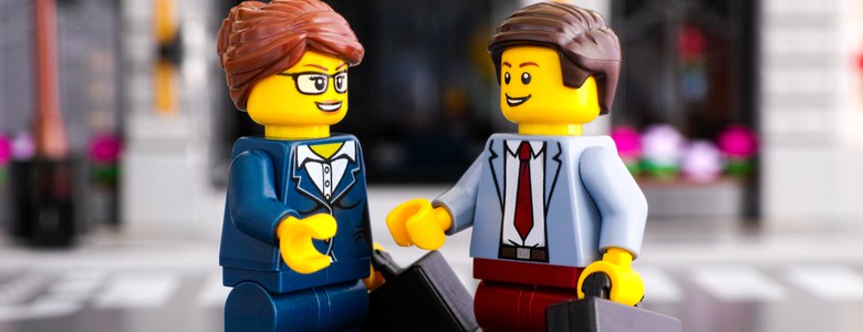 A Lego man and woman shaking hands and holding briefcases