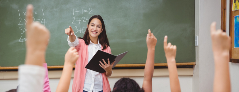 A teacher at the front of a maths class with pupils’ hands raised